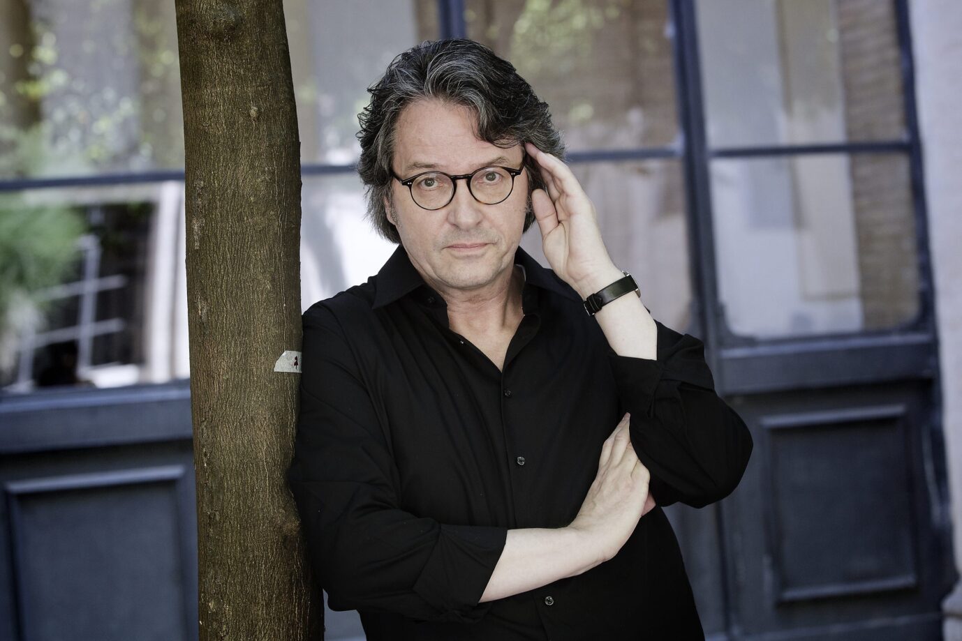 Der Schriftsteller Ralf Rothmann lehnt sich an einen Baum an und hält nachdenklich den Kopf in den Händen.