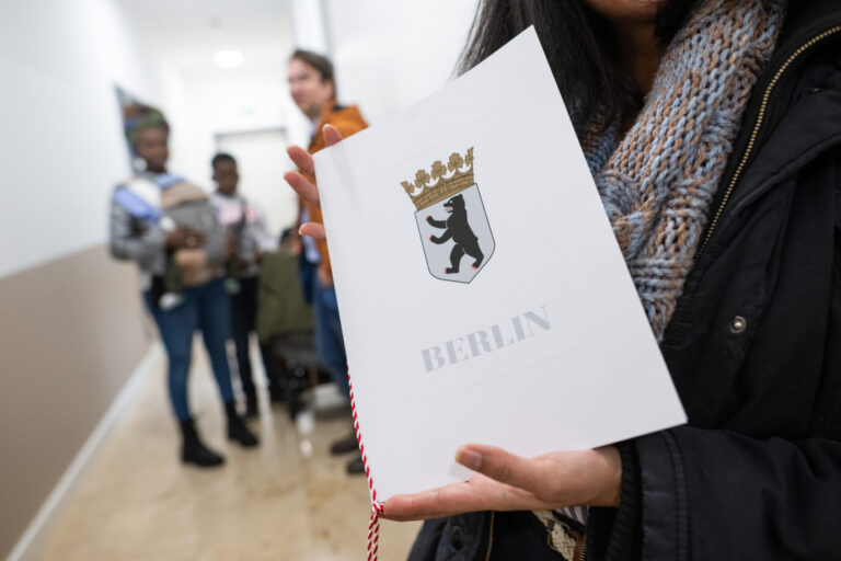 Eine Frau zeigt im Landesamt für Einwanderung ihre Einbürgerungsurkunde mit dem Wappen Berlins.