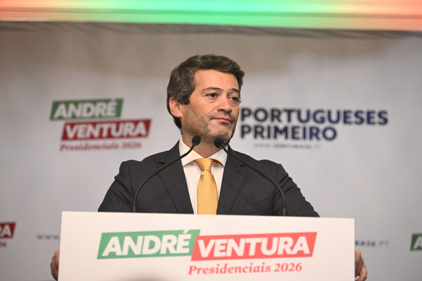 Chega-Chef André Ventura steht an einem Rednerpult und schaut konstatiert drein