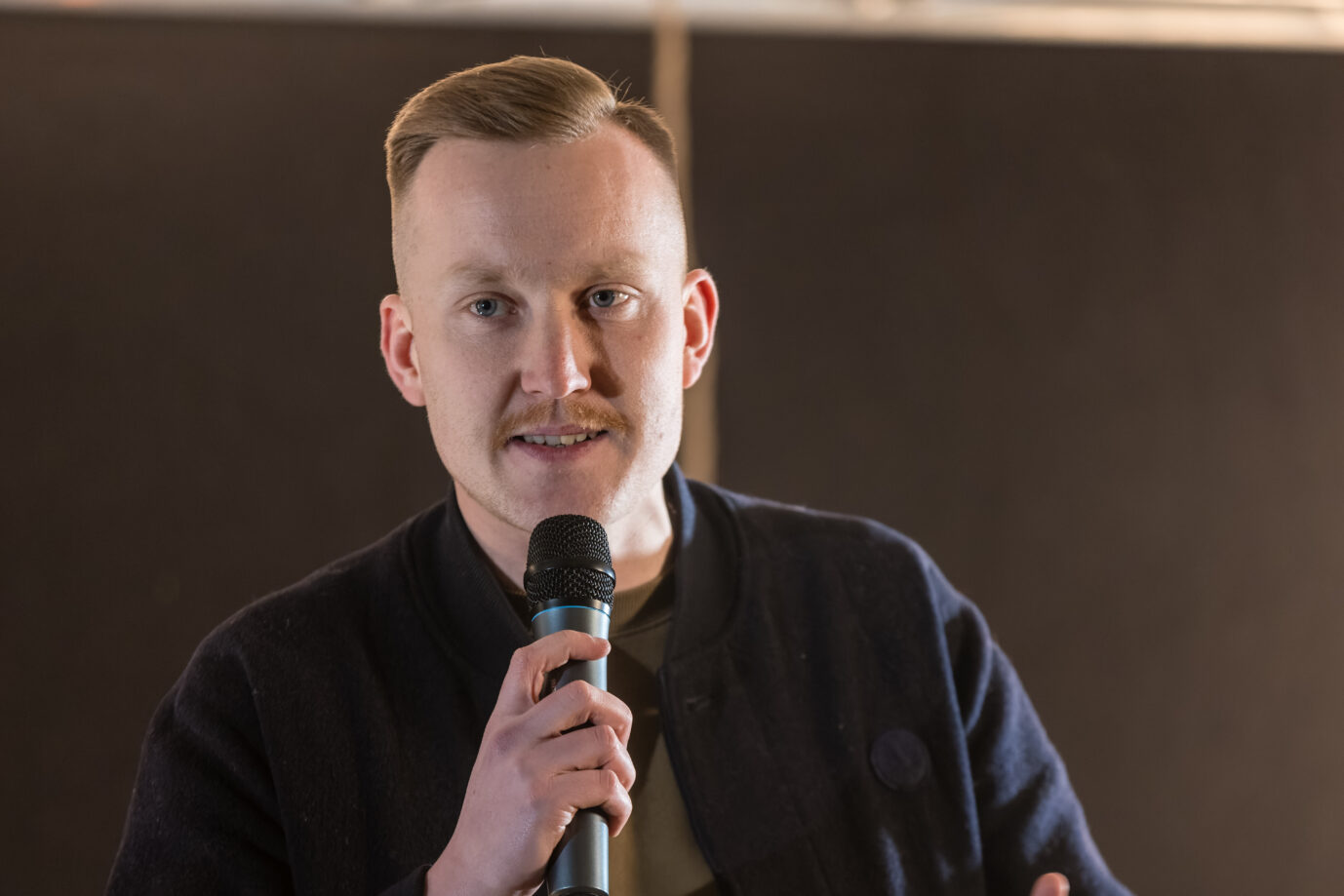 Ein Mann hält in einem Innenraum ein Handmikrofon und spricht zu einem Publikum. Maximilian Märkl nimmt an einem von Martin Sellner organisierten Podium zum Thema Remigration teil. Maximilian Märkl bei einer Veranstaltung in Augsburg: Der Bundessprecher der Identitären Bewegung tritt aus der AfD aus. Foto: picture alliance/dpa | Frank Hammerschmidt