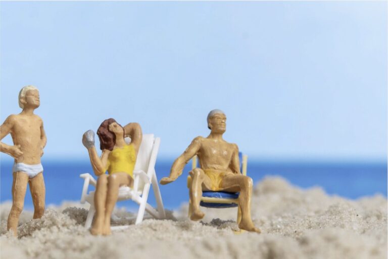 Kleine Plastikfiguren stehen im Sand und sitzen auf Camping-Stühlen – Symbolbild für Glück