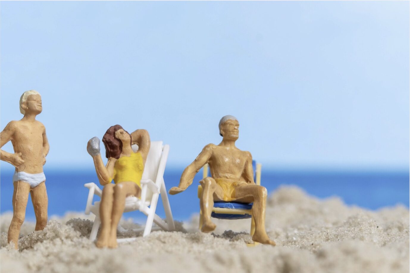 Kleine Plastikfiguren stehen im Sand und sitzen auf Camping-Stühlen – Symbolbild für Glück