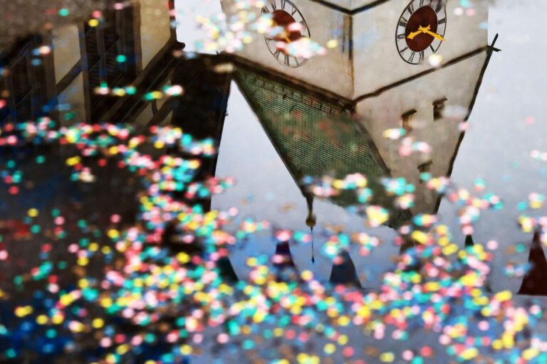 Das Bild zeigt eine Pfütze voller Konfetti, in der sich eine Kirche spiegelt.