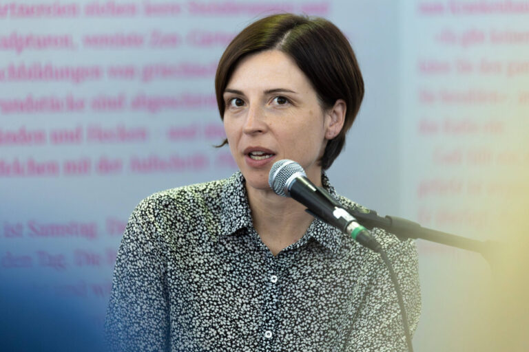 Die Schriftstellerin und Trägerin des Deutschen Buchpreises Dorothee Elmiger trägt ein schwarz-weiß gepunktetes Hemd, eine Kurzhaarfrisur und spricht in ein Mikrofon