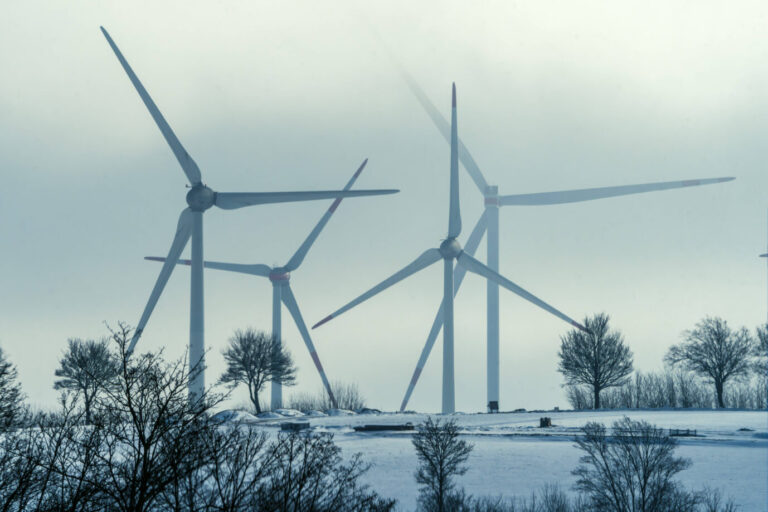 In einer winterlich verschneiten Landschaft drehen sich Windräder – Symbolbild für die Energiewende