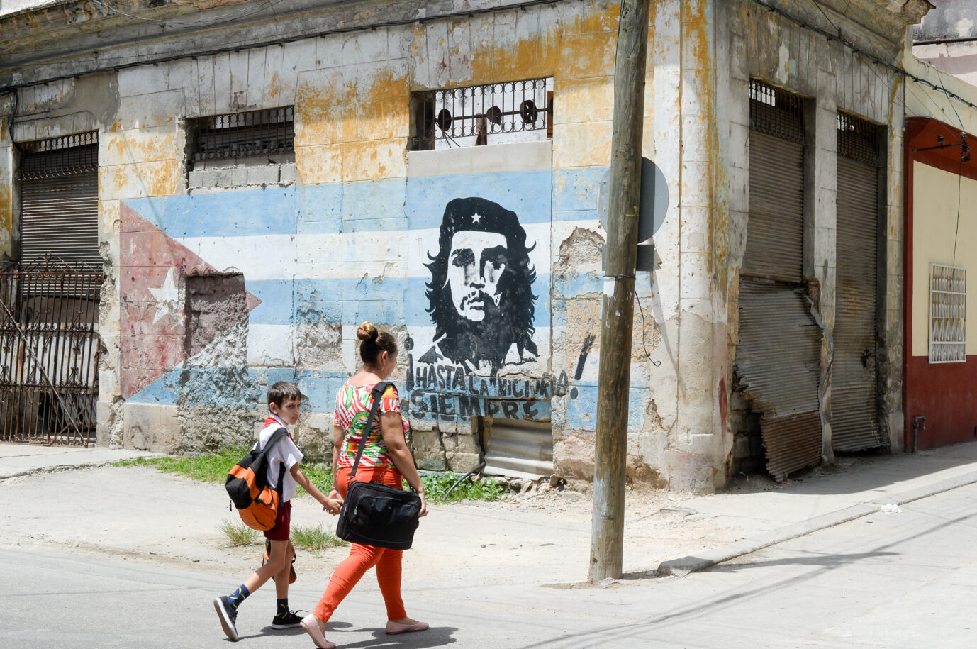 22.06.2018, Kuba, Havanna: Passanten gehen an einem Graffito von Che Guevara auf einer kubanischen Flagge an einer Ecke in der Altstadt vorbei. In Havanna befindet sich die größte erhaltene koloniale Altstadt Lateinamerikas. Im Jahr 2019 feiert die Stadt sein 500. Gründungsjubiläum. Foto: Jens Kalaene/dpa-Zentralbild/dpa