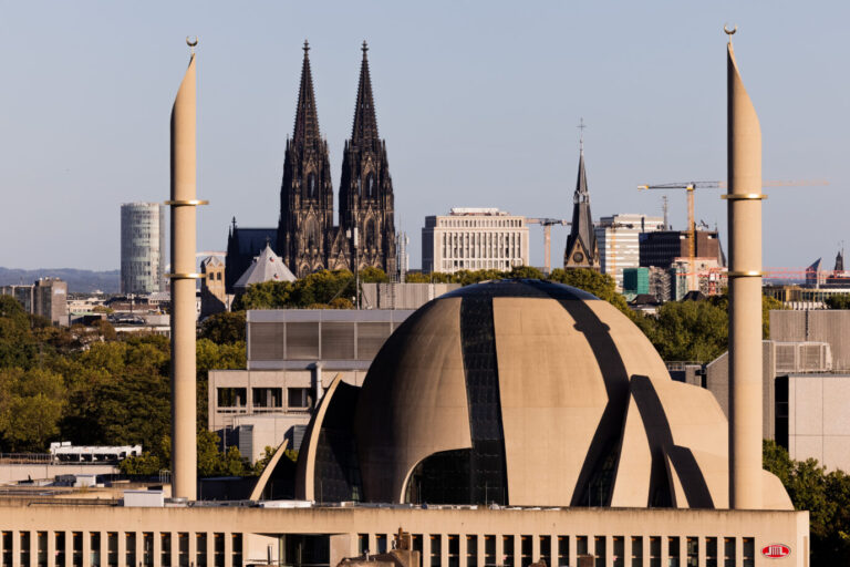 Sonnenlicht fällt auf die DITIB-Zentralmoschee in Köln, dahinter ist der Kölner Dom zu sehen – Verhältnis zwischen Islam und Christentum