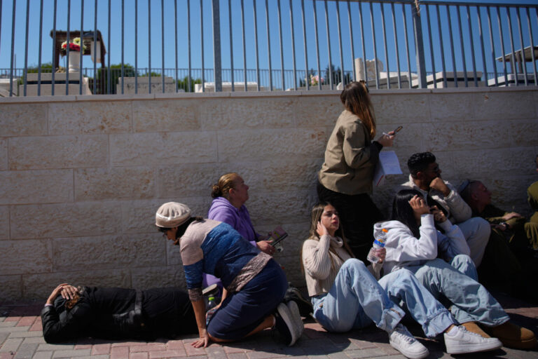 Mourners take cover while air-raid sirens warn of incoming missiles launched by Iran toward Israel during the funeral of Sarah Elimelech and her daughter Ronit who were killed in an Iranian missile attack, in Beit Shemesh, Israel, Monday, March 2, 2026. (AP Photo/Ohad Zwigenberg)