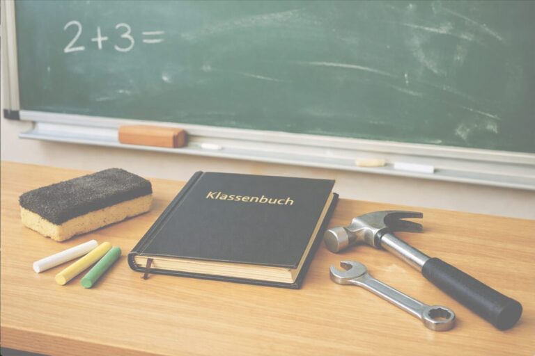 Auf einem Schulpult liegen Schulutensilien und daneben ein Hammer – Symbolbild für "LifeTeacher"