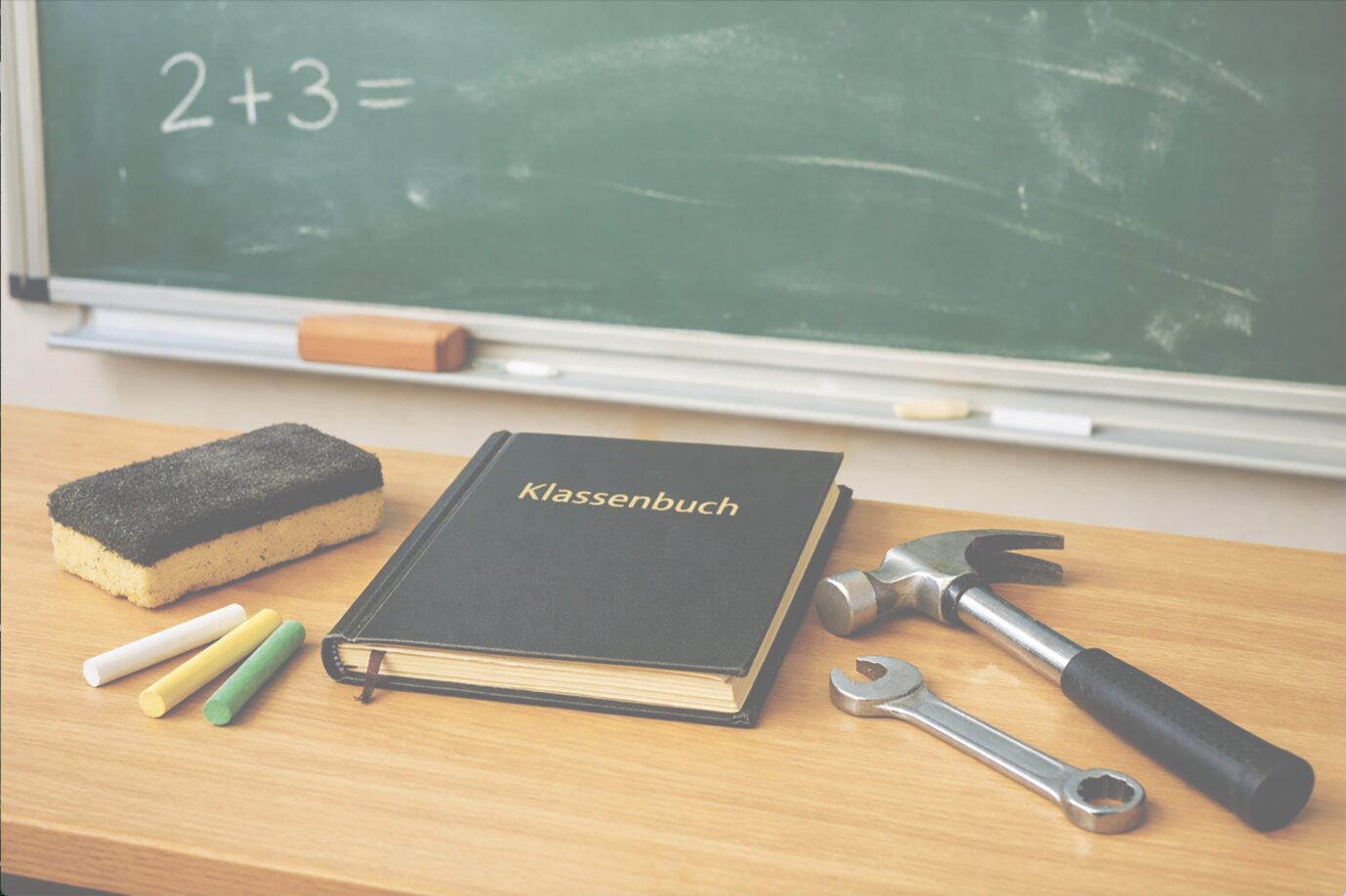 Auf einem Schulpult liegen Schulutensilien und daneben ein Hammer – Symbolbild für "LifeTeacher"