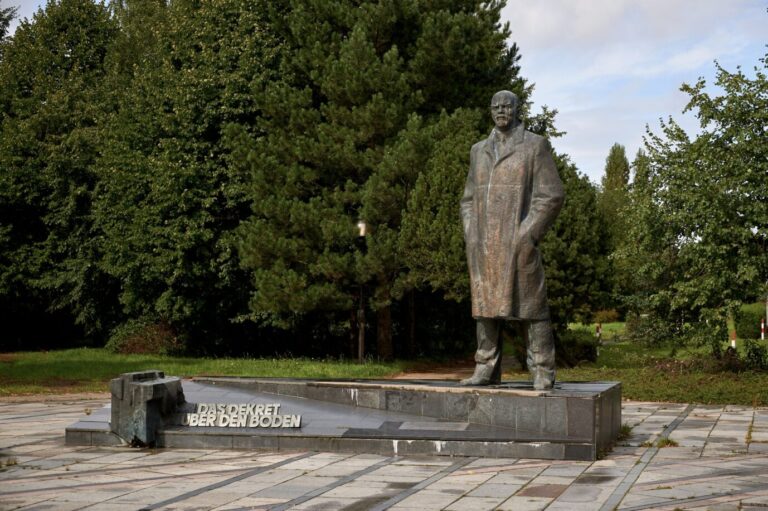 Auf einer grauen Steinfläche steht eine Bronzestatue von Lenin aus der DDR