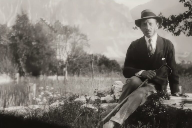 Der Dichter Rainer Maria Rilke sitzt auf einer Steinmauer und schaut in die Kamera