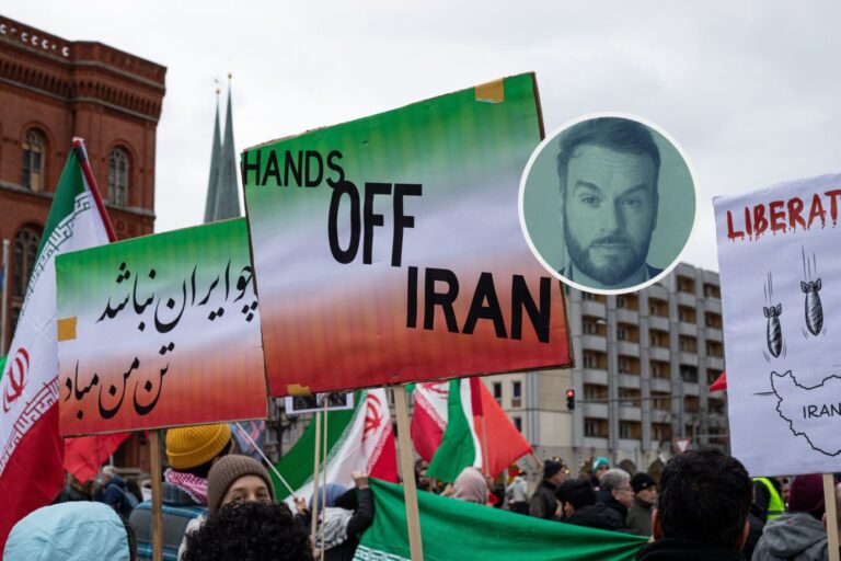 Aufnahme einer Demonstration am 15. März 2026 in Berlin vor dem Roten Rathaus, bei der Teilnehmer mit iranischen Nationalflaggen und Plakaten mit der Aufschrift „Hands off Iran“ sowie persischsprachigen Losungen zu sehen sind. Im Hintergrund sind weitere Protestschilder, darunter eines mit der Forderung nach Befreiung des Irans und einer Zeichnung von Bomben, die auf das Land fallen. Die Kundgebung fand im Kontext der eskalierenden Spannungen zwischen Iran, Israel und den USA statt, wobei sowohl regimefreundliche als auch regimkritische Gruppen anwesend waren. Demonstration vor dem Roten Rathaus: Teilnehmer mit Plakat „Hands off Iran“. Foto: picture alliance / ZUMAPRESS.com | Michael Kuenne
