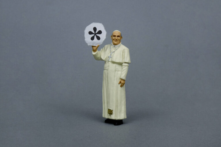 Figur eines Papstes in weißer Soutane hält eine Tafel mit einem schwarzen Genderstern vor grauem Hintergrund. Bezug zur Debatte über geschlechtergerechte Sprache in kirchlichen Texten, etwa der „Bibel in gerechter Sprache“. Papstfigur mit Genderstern: Auch vor der Bibel macht die Gendersprache nicht halt. Foto: IMAGO / Steinach