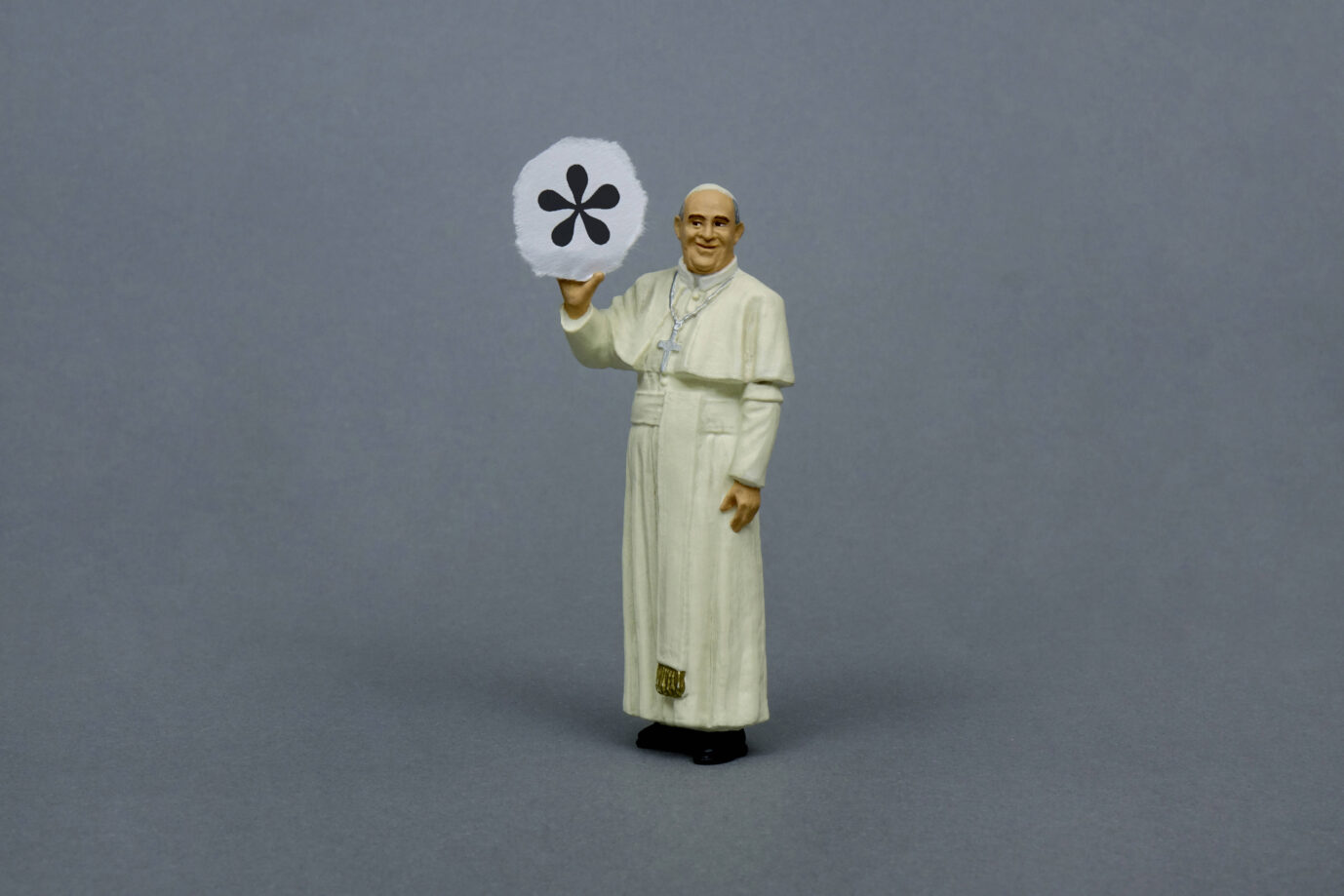 Figur eines Papstes in weißer Soutane hält eine Tafel mit einem schwarzen Genderstern vor grauem Hintergrund. Bezug zur Debatte über geschlechtergerechte Sprache in kirchlichen Texten, etwa der „Bibel in gerechter Sprache“. Papstfigur mit Genderstern: Auch vor der Bibel macht die Gendersprache nicht halt. Foto: IMAGO / Steinach