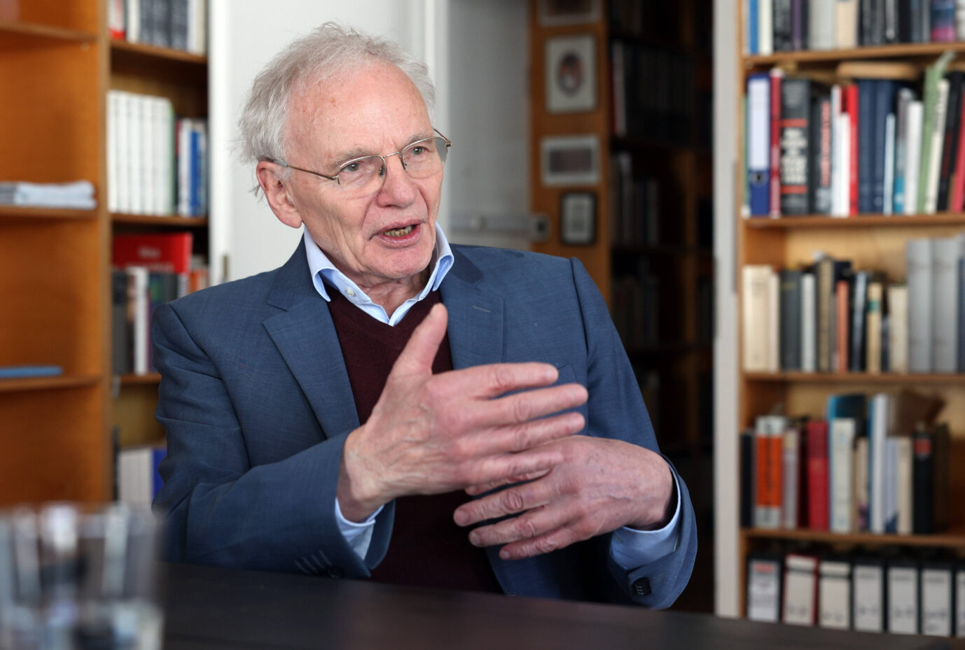 Der Historiker Götz Aly sitzt vor einer Bücherwand und gestikuliert mit den Händen.