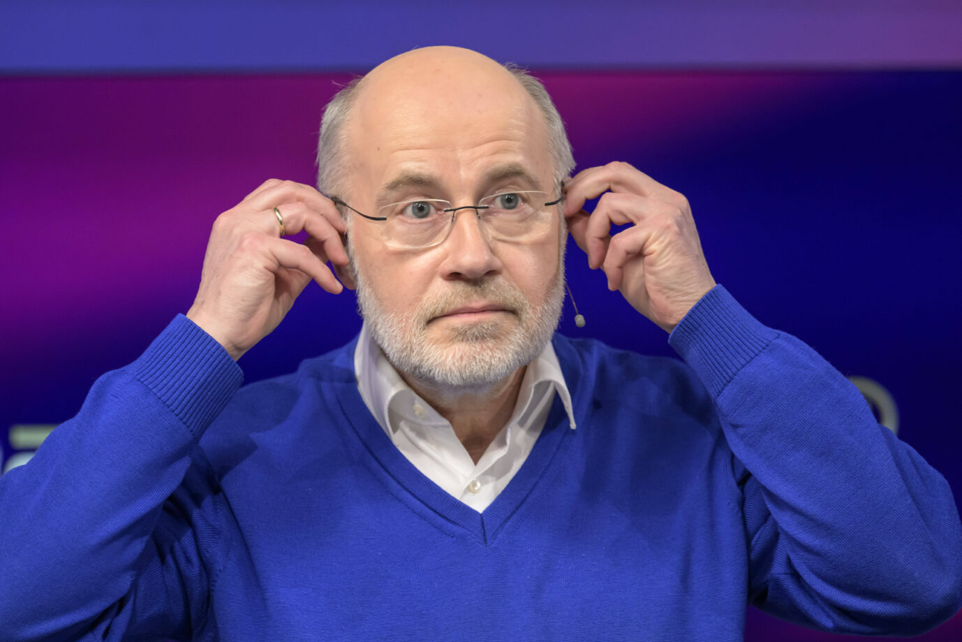 Der Wissenschaftsjournalist Harald Lesch trägt einen blauen Pullover und greift sich an die Brille