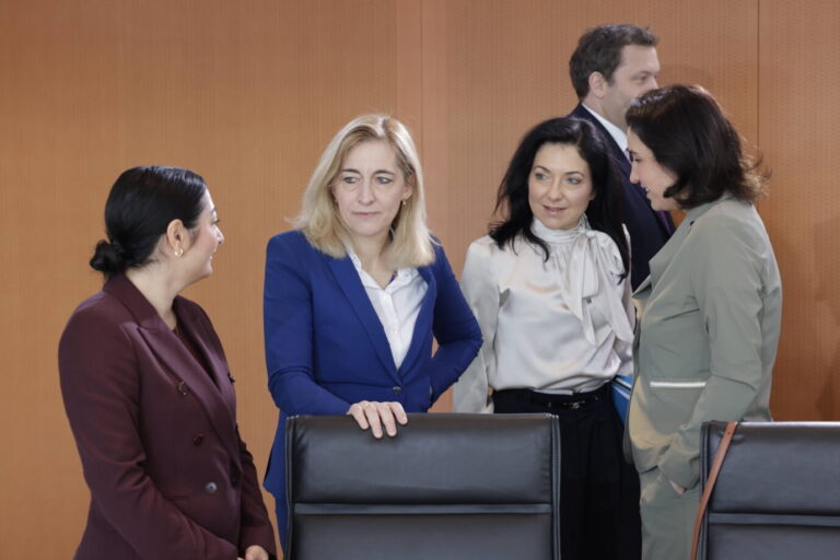 Vier Minister stehen in einem Sitzungssaal dicht beieinander und sprechen miteinander. Zwei von ihnen lächeln. Sie tragen dunkle Anzüge und Kostüme. Im Hintergrund steht ein weiterer Mann und blickt in ihre Richtung. Die Bundesminister Alabali Radovan, Warken, Reiche und Bär bei einer Kabinettssitzung, im Hintergrund Klingbeil: Auch die schwarz-rote Bundesregierung gibt eine hohe fünfstellige Summe für Visagisten und Frisöre aus. Foto: IMAGO / Metodi Popow