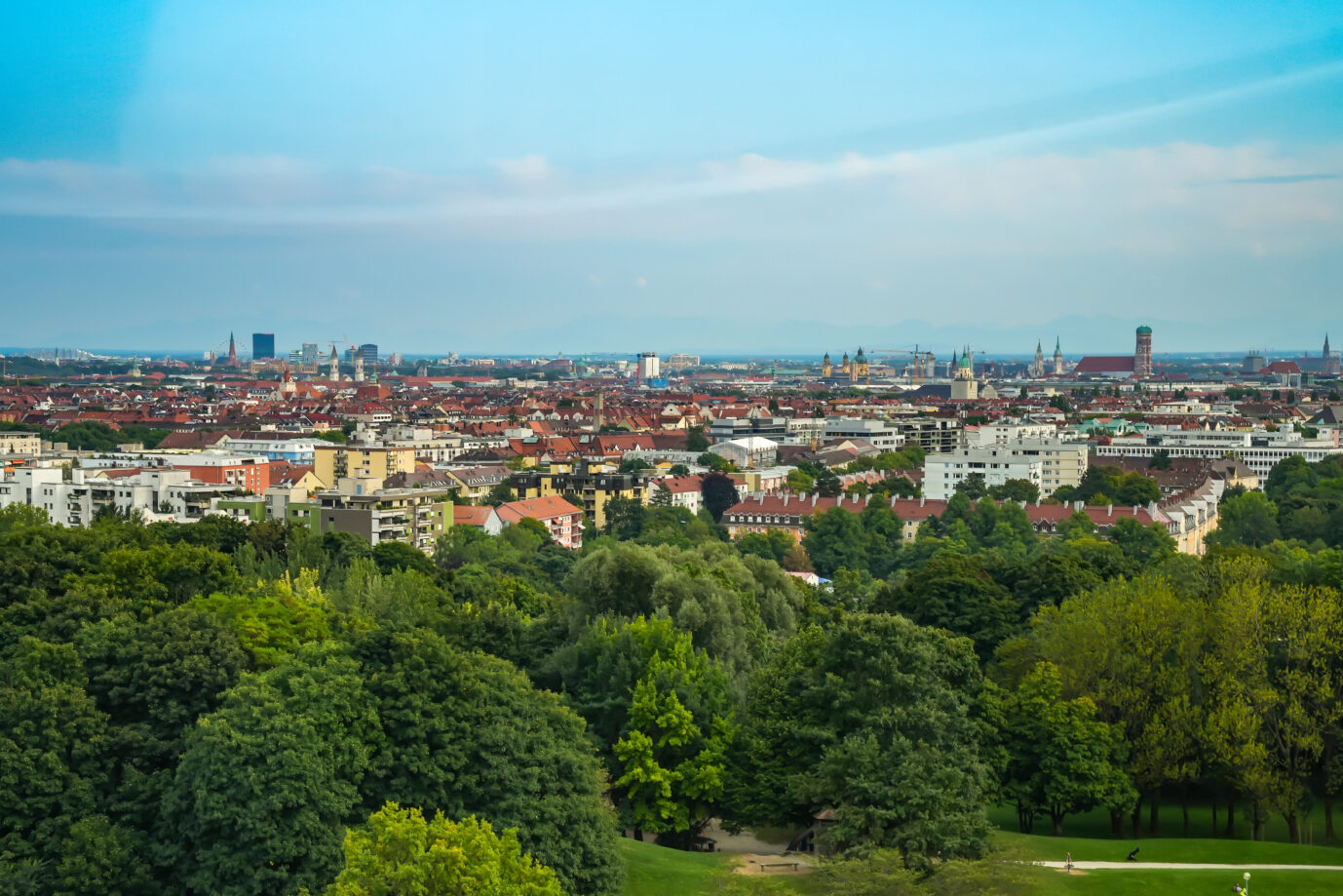 Panoramablick über die Stadt München, Bayern, Deutschland, nach Süden. Skyline von München mit seinen berühmten Wahrzeichen. Im Vordergrund Bäume im Olympiapark. Foto:picture alliance / CHROMORANGE | Sandra Alkado