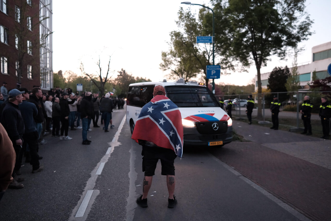 Ein Mann mit einer umgehängten Südstaatenflagge stellt sich gegen ein Polizeiauto – er protestiert gegen Asylbewerber in den Niederlanden