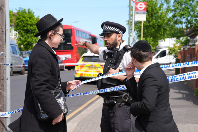 Ein Mann in der Uniform der britischen Polizei spricht mit zwei Jungen, die in der Art orthodoxer Juden gekleidet sind – in London gab es zuvor einen antisemitischen Messerangriff