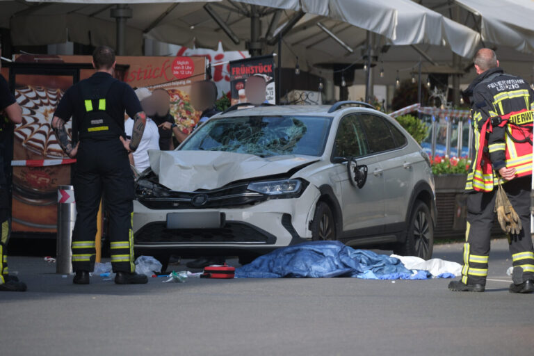 Einsatzkräfte und weitere Personen stehen um ein beschädigtes Auto. In Leipzig ist ein Auto in mehrere Menschen gefahren. Nach Angaben der Polizei gibt es mehrere Verletzte.