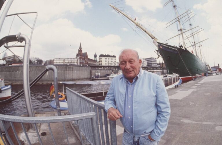 Man sieht den Schriftsteller James Krüss, wie er am Hafen von Helgoland an einem Geländer lehnt