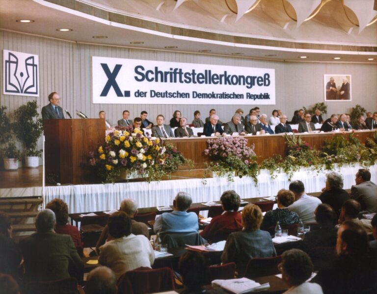 In einem kargen Raum sitzen Menschen auf einer Bühne, davor Zuschauer: Es handelt sich um den DDR-Schriftstellerkongress am 24. November 1987 in Ost-Berlin