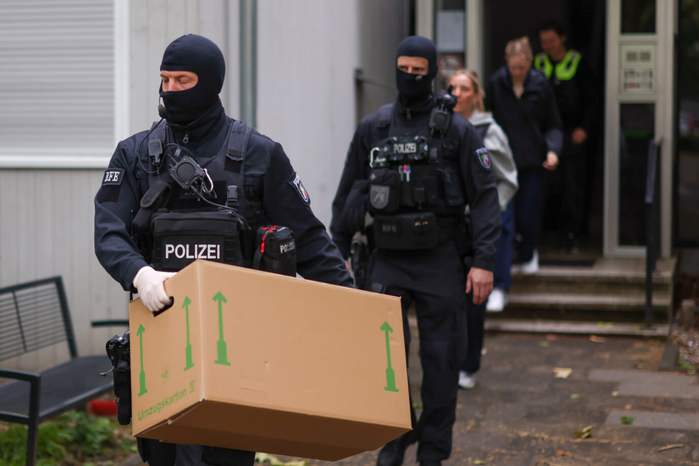 Vermummte Polizisten verlassen bei einem Einsatz ein Gebäude mit sichergestellten Gegenständen. Zwei Monate nach der eskalierten Feier einer Großfamilie in Leverkusen geht die Polizei mit Razzien gegen die mutmaßlichen Rädelsführer vor. Seit dem frühen Morgen werden nach dpa-Informationen mehrere Objekte durchsucht. Vermummte Polizisten während einer Razzia (Symbolbild): Bei den Hausdurchsuchungen gegen die mutmaßlichen IS-Anhänger gab es keine Verhaftungen. Foto: picture alliance/dpa | Christoph Reichwein