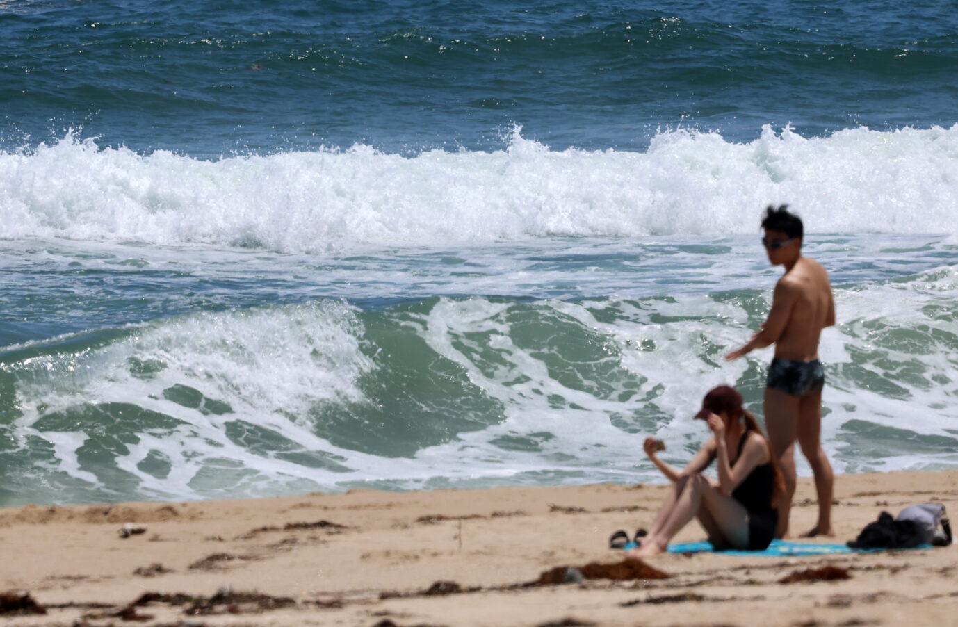 Ein Mann und eine Frau, also zwei Urlauber, stehen am Strand, im Hintergrund schäumen Wellen – viele Deutsche können sich solche Reisen aber nicht leisten