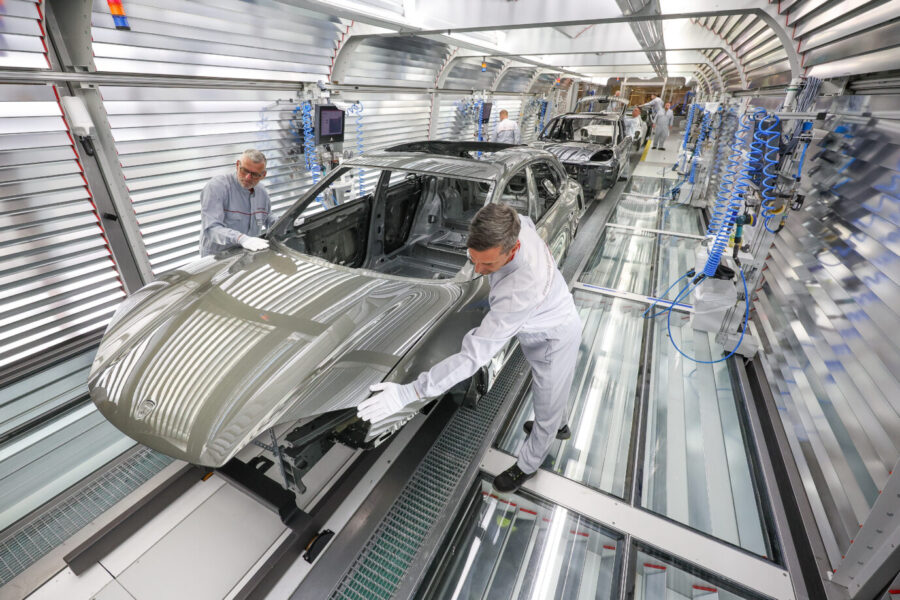 Zwei Porsche-Mitarbeiter prüfen in der Lackiererei den Lack der Karosserie eines vollelektrischen Porsche Macan. Vor allem der Elektromarkt macht dem Hersteller Probleme. Foto: picture alliance/dpa | Jan Woitas