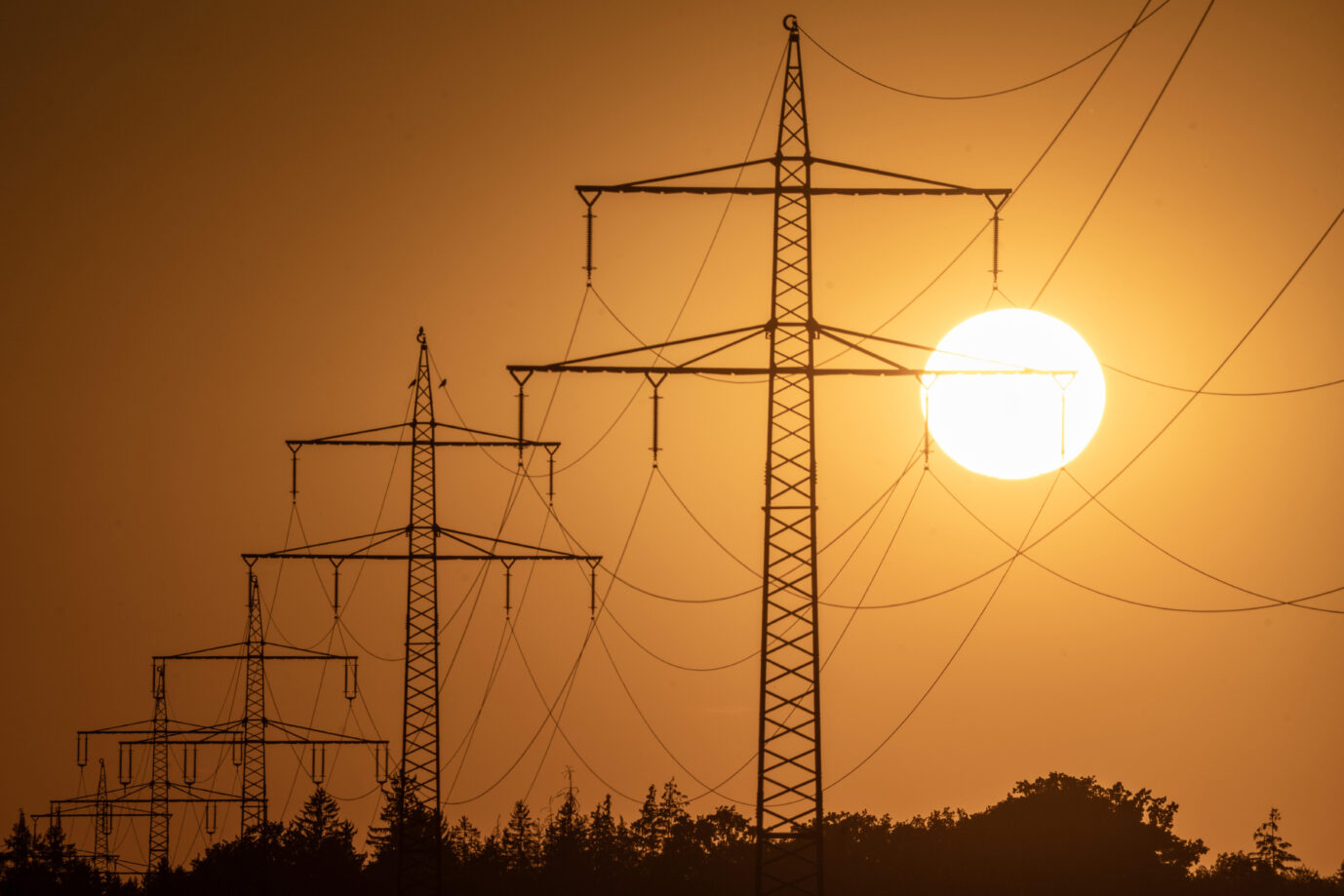 Eine helle Sonne scheint über schemenhaft erkennbaren Strommasten