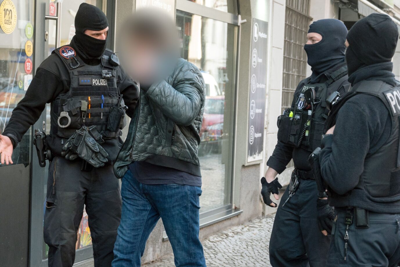 Ein Mann (2.v.l.) diskutiert mit Polizisten, die bei einer Razzia vor einem Laden stehen. Mit einer Großrazzia ist die Polizei am Donnerstag gegen Clankriminalität in Berlin und Umgebung vorgegangen.