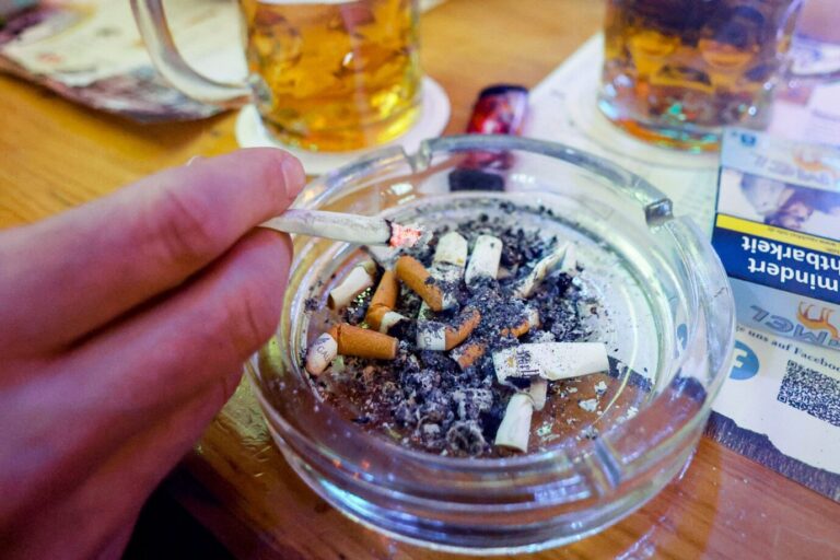 Das BIld zeigt einen Aschenbecher mit Zigaretten und dazu Bier in einer Kneipe.