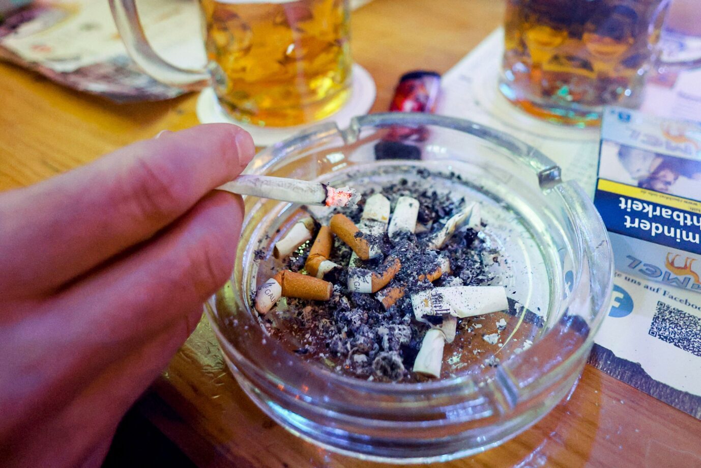 Das BIld zeigt einen Aschenbecher mit Zigaretten und dazu Bier in einer Kneipe.