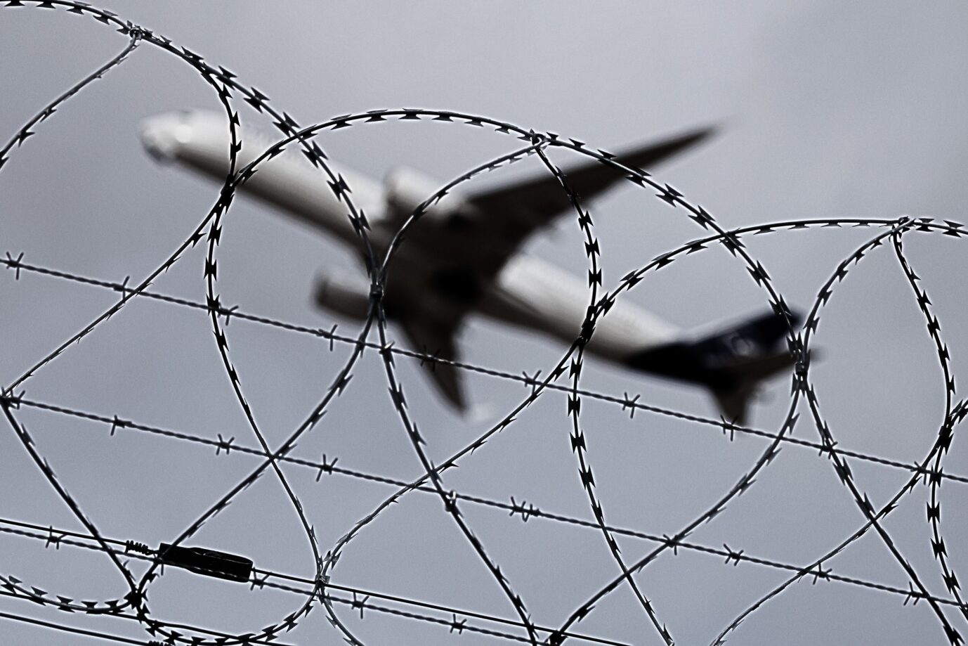 Das Bild zeigt ein abhebendes Flugzeug hinter einem Stacheldrahtzaun. Es ist ein Symbolbild für einen journalistischen Text über die Migrationswende der Bundesregierung.