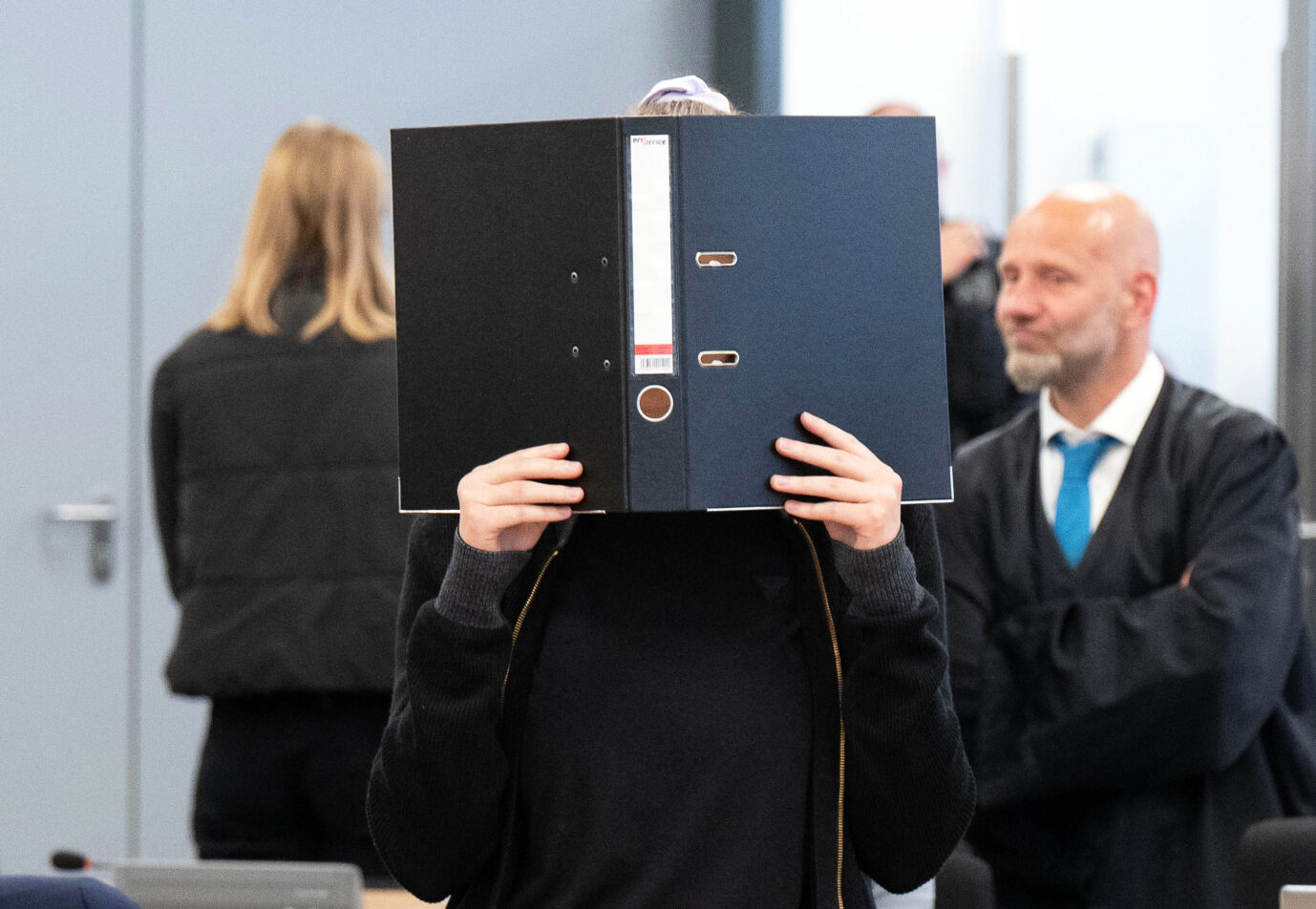 Die Angeklagte Lina E. steht bei der Fortsetzung des Prozesses im Oberlandesgericht (OLG) Dresden im Verhandlungssaal und hält einen Aktenordner vor ihr Gesicht. Das Oberlandesgericht hat die mutmaßliche Linksextremistin Lina E. zu fünf Jahren und drei Monaten Freiheitsstrafe verurteilt. Nach Auffassung des Gerichts gehörte sie einer Gruppe an, die Überfälle auf Mitglieder der rechten Szene begangen hat. Sie war ein wichtiger Teil der sogenannten Hammerbande.(Recrop)