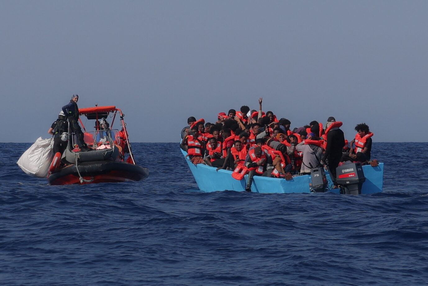 Migranten an Bord eines überfüllten Bootes reagieren, als sie während einer Rettungsaktion in der Such- und Rettungszone (SAR) im zentralen Mittelmeer vor der Küste Libyens am 11. August 2025 von der Besatzung des von der deutschen Nichtregierungsorganisation Sea-Watch betriebenen Such- und Rettungsschiffs „Sea-Watch 5“ angefahren werden. Das Such- und Rettungsschiffs „Sea-Watch 5“ fährt auf ein Boot voll Migranten zu (Symbolbild): Italiens Vize-Ministerpräsident Salvini will, dass Deutschland seine Schlepper-NGOs „zurückpfeift“. Foto: picture alliance / REUTERS | Louisa Gouliamaki