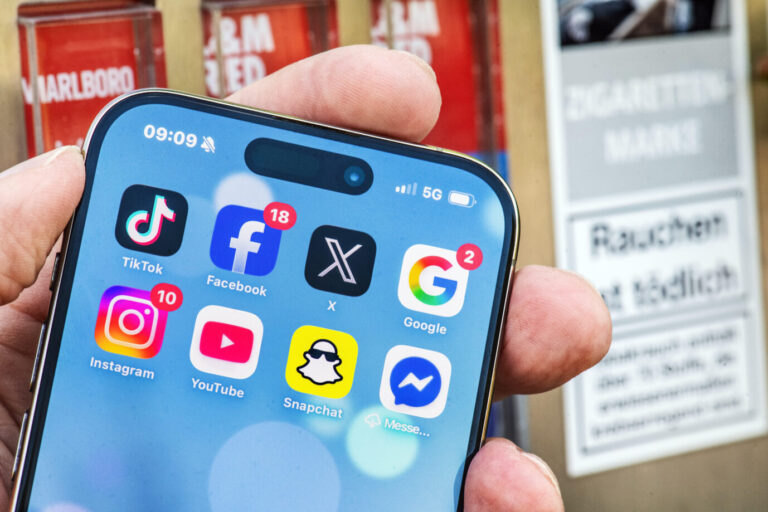 Deutschland, München, Juni 2026, Social-Media-Verbot für Kinder und Jugendliche, Vergleich mit Rauchen und Tabakindustrie, wo ein Jugendschutz gilt, Symbolfoto, Handy mit u.a. wichtigen Social Media Apps vor einem Zigarettenautomaten mit Hinweis Rauchen ist tödlich, Tabakwaren dürfen nicht an unter 18jährige abgegeben werden, Vergleich: Rauchen macht genauso süchtig wie Social Media Konsum, nach Verbot in Australien gibt es in vielen Ländern, auch in Deutschland, eine Diskussion, ein Mindestalter für die Nutzung von Social Media einzuführen, Nutzung z. B. von TikTok und Instagram altersmäßig zu begrenzen, die psychische Gesundheit von Kindern und Jugendlichen zu schützen, Bildung, Erziehung, Bayern,. Apps auf dem Smartphone (Symbolbild): Die Direktorin der Landesmedienanstalt will Plattformen dazu zwingen, „journalistische Public-Value-Inhalte“ zu bevorzugen. Foto: picture alliance / Wolfgang Maria Weber | Wolfgang Maria Weber