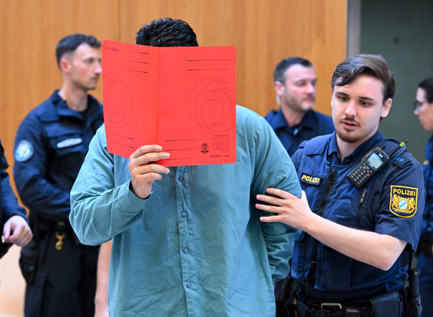 Der Angeklagte Farhad N. wird zu Prozessbeginn von Polizeibeamten in den Prozesssaal geführt. Farhad N.: Das Oberlandesgericht München stellte es eine besondere Schwere der Schuld fest. Foto: picture alliance/dpa | Sven Hoppe. In Verdi-Demo gerast