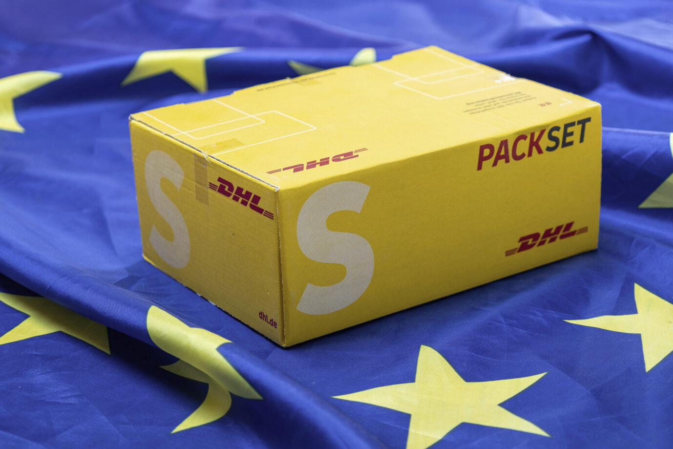 Symbolbild Verpackungsverordnung: DHL-Päckchen auf einer Flagge der Europäischen Union