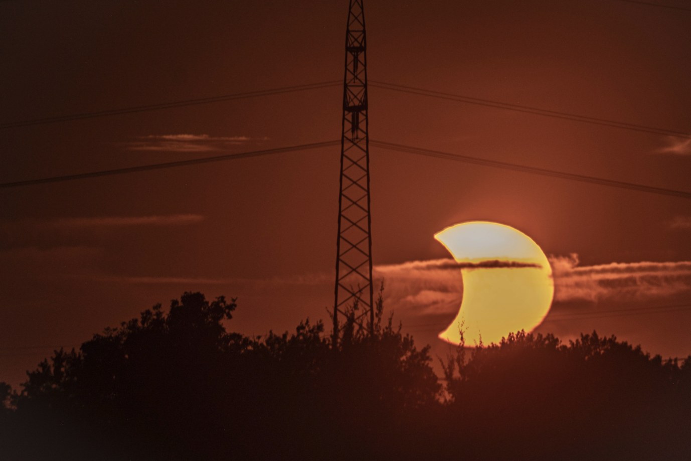 Symbolbild für den Hitze-Juli und die Erneuerbaren Energien: Sonnenuntergang vor einem Strommast in Niedersachsen. Foto: IMAGO / Norbert Neetz