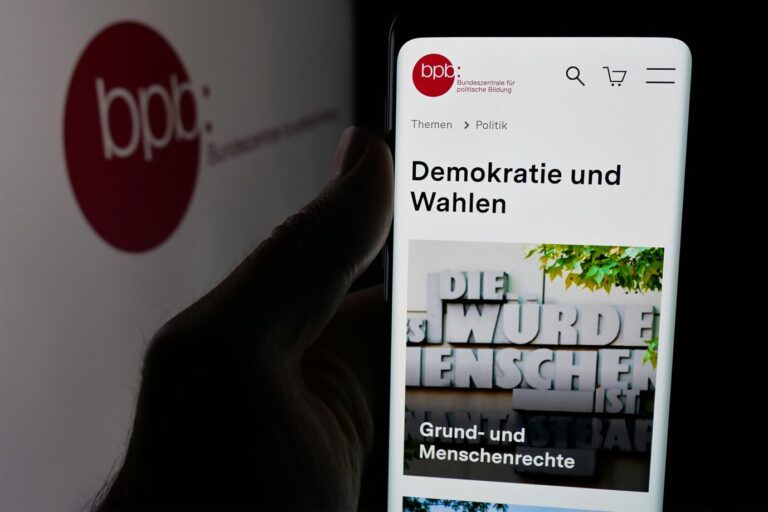In this photo illustration, a person is holding a smartphone with the web page of Bundeszentrale für politische Bildung (bpb) on screen in front of logo. (Photo by Timon Schneider / SOPA Images/Sipa USA) *** Strictly for editorial news purposes only *** Die Bundeszentrale für politische Bildung setzt Israel-Studienreisen nur auf Grund der Reisewarnungen des Auswärtigen Amtes aus (Symbolbild). Foto: picture alliance / Sipa USA | SOPA Images