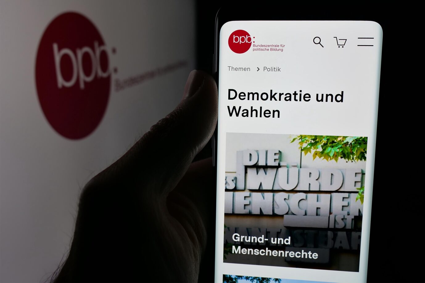 In this photo illustration, a person is holding a smartphone with the web page of Bundeszentrale für politische Bildung (bpb) on screen in front of logo. (Photo by Timon Schneider / SOPA Images/Sipa USA) *** Strictly for editorial news purposes only *** Die Bundeszentrale für politische Bildung setzt Israel-Studienreisen nur auf Grund der Reisewarnungen des Auswärtigen Amtes aus (Symbolbild). Foto: picture alliance / Sipa USA | SOPA Images