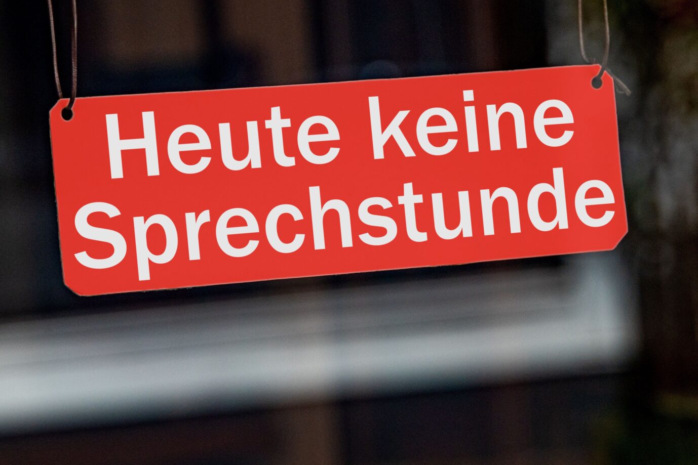 [M] Ein symbolisches, rotes Schild mit der Aufschrift "Heute keine Sprechstunde" haengt leicht schraeg an Lederbaendern in einem Fenster. Foto mit Composing als Symbolbild fuer den Ausfall von Sprechstunden bei Hausaerzten, Kinderaerzten, Zahnaerzten, ... z.B. durch Krankheit oder Personalmangel.
