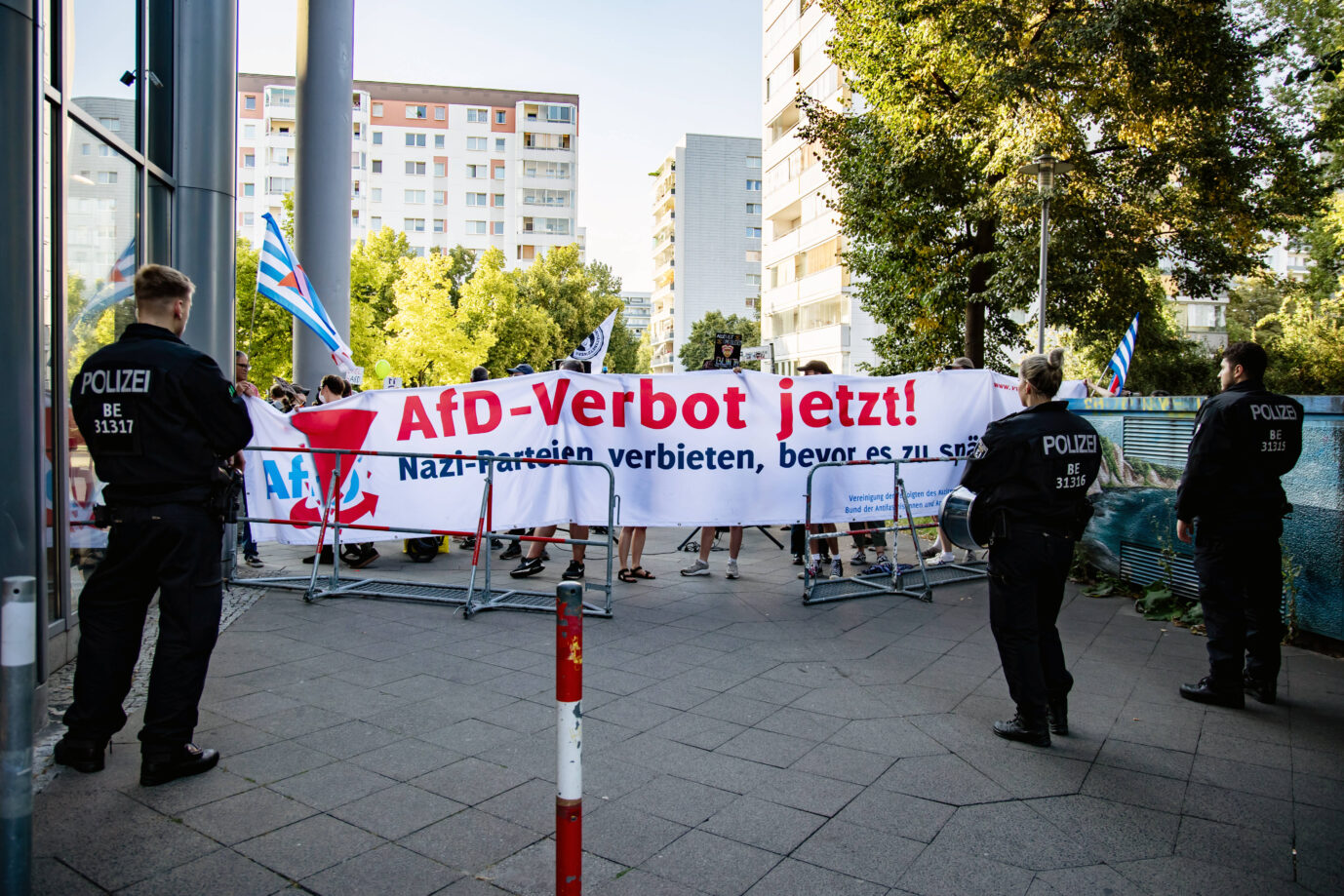 Polizisten stehen vor einer Gruppe Linksextremer, die ein Transparent gegen die AfD hochhalten