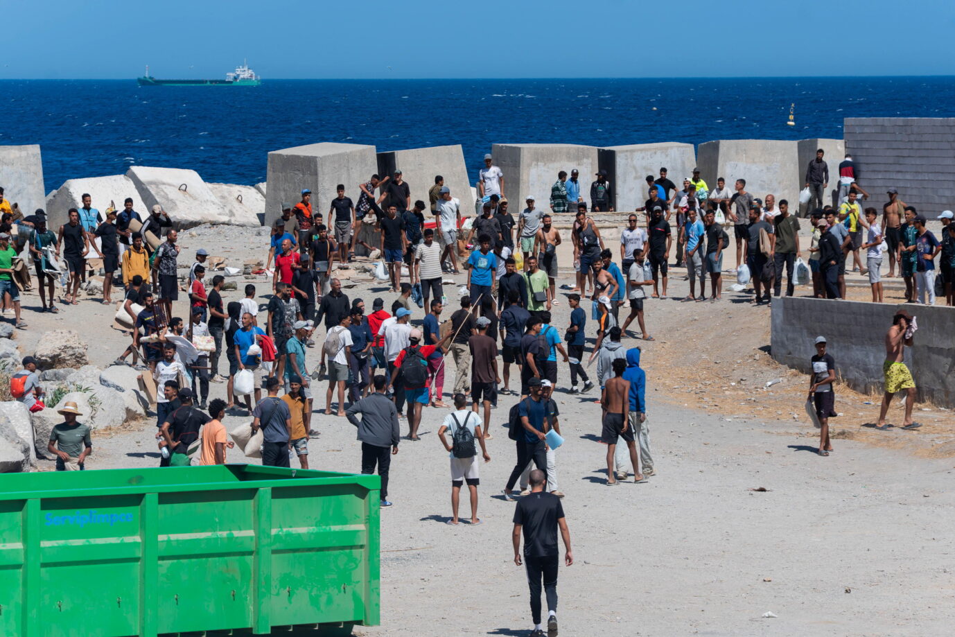 Auf einer großen Betonfläche sieht man eine große Gruppe junger nordafrikanischer Männer – es handelt sich um Migranten in Ceuta