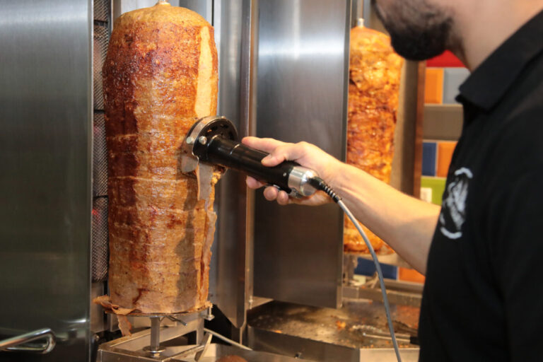 Ein Mann steht in einem Dönerladen und säbelt Fleisch von einem Dönerspieß